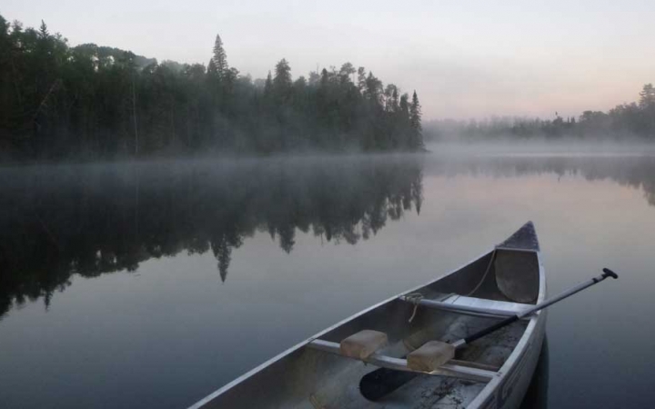 an empty canoe sits in still water at dawn while fog rests just above the surface
